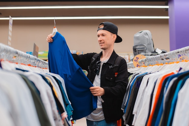 Foto retrato sonriente joven moderno hipster hombre de 25-35 años de edad cap de compras en mens tienda de ropa, ropa, prendas de vestir, vestimenta, vestimenta