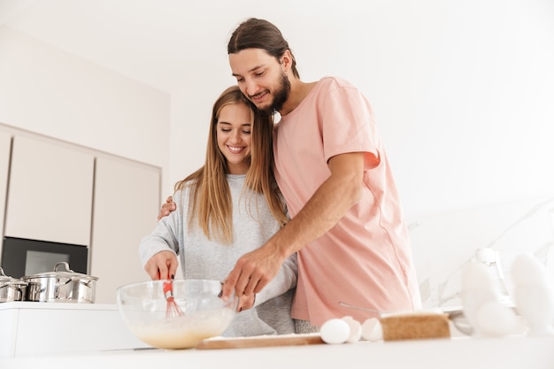 Retrato de sonriente joven pareja amorosa en la cocina en el interior en casa cocinando juntos.