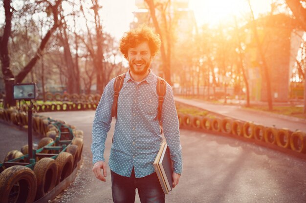 Retrato sonriente joven rizado rojizo posando cerca de un camino de neumáticos en el parque