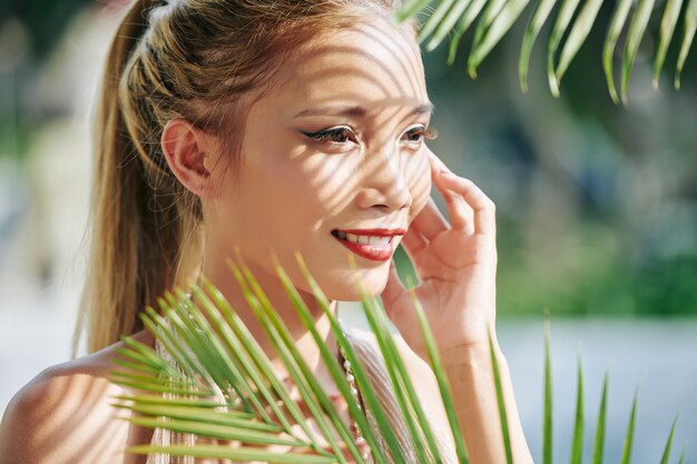 Retrato de sonriente joven vietnamita con largas pestañas de pie al aire libre