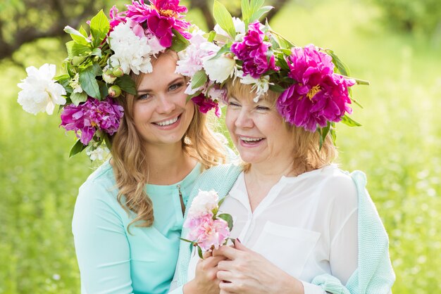 Retrato de sonriente madre e hija posando y abrazando en coronas de flores al aire libre. El concepto de familia. La relación entre madre e hija.