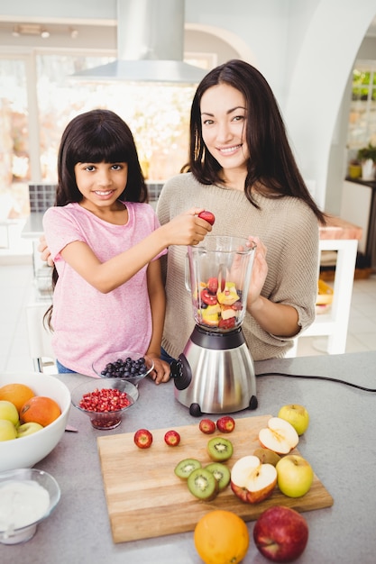 Retrato de sonriente madre e hija preparando zumo de fruta