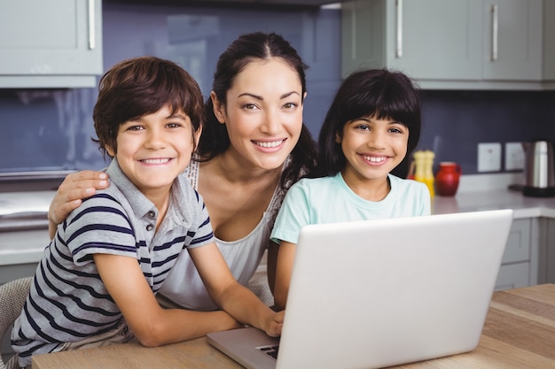 Retrato de sonriente madre e hijos usando una computadora portátil