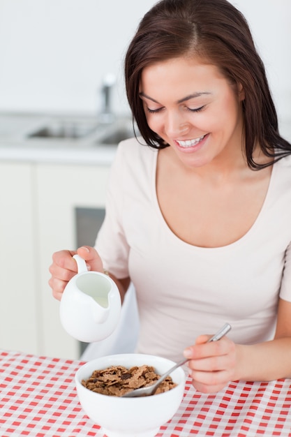 Retrato de una sonriente morena vertiendo leche en su cereal