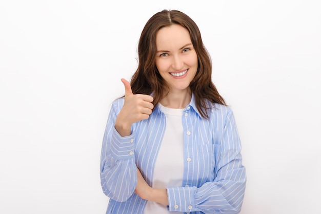 Retrato sonriente de mujer con camisa azul muestra gestos pulgares hacia arriba sobre fondo blanco