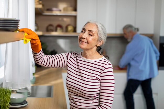 Foto retrato, de, sonriente, mujer mayor, limpieza, estantes, en, cocina, de, polvo