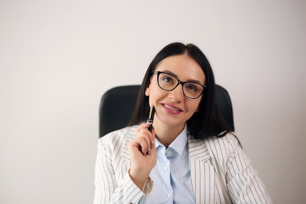 Retrato de sonriente mujer de negocios bastante joven en gafas sentado en el lugar de trabajo.