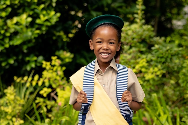 Retrato de una sonriente niña exploradora afroamericana en uniforme con mochila contra las plantas