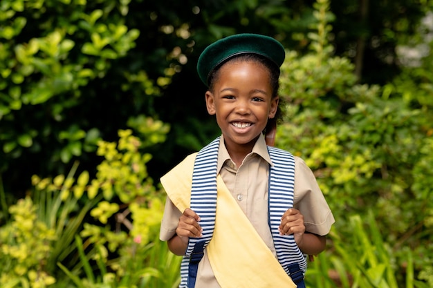 Foto retrato de una sonriente niña exploradora afroamericana en uniforme con mochila contra las plantas