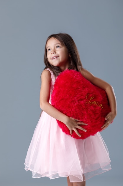 Retrato de sonriente niña linda en vestido rosa con gran corazón rojo