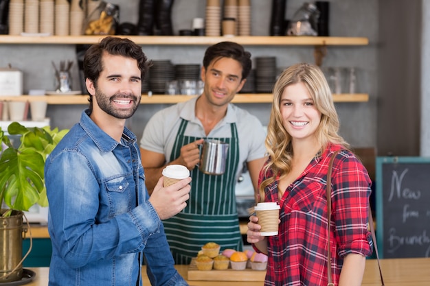 Retrato de la sonriente pareja de pie en el mostrador con taza de café