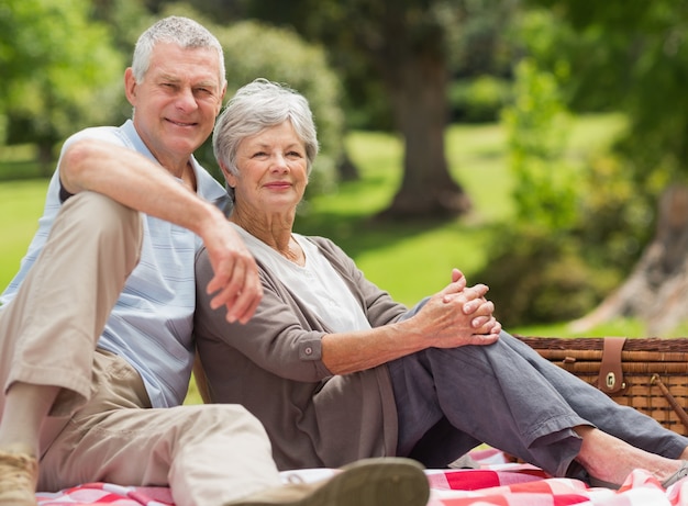 Retrato de una sonriente pareja senior sentado con cesta de picnic en el parque