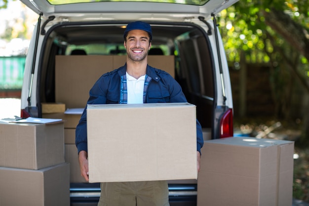 Foto retrato de sonriente repartidor llevando caja de cartón