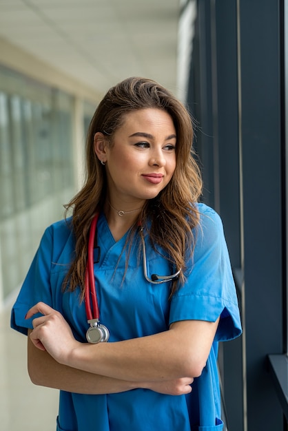 Retrato de sonriente trabajadora médica en uniforme azul con estetoscopio en la clínica.