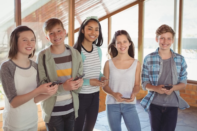 Retrato de sonrientes amigos de la escuela mediante teléfono móvil en el corredor