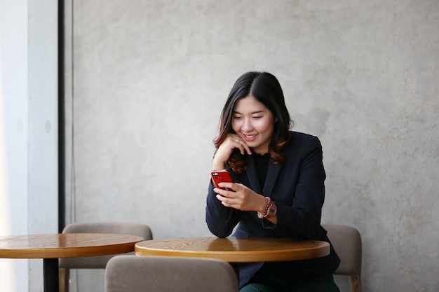 El retrato de la sonrisa joven de la mujer asiática mira el teléfono móvil