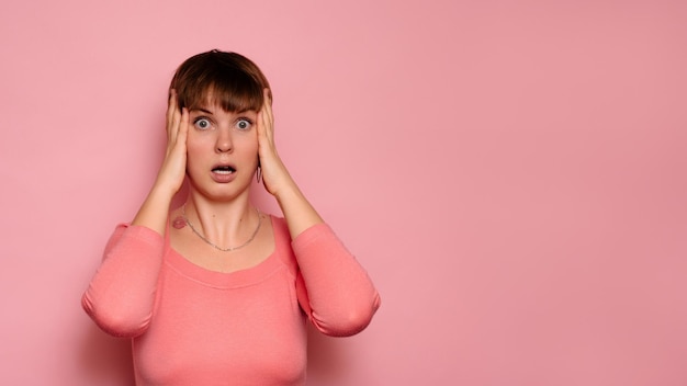 Retrato de una sorprendida y atractiva chica caucásica aislada en un fondo rosa sosteniendo su cabeza con las manos asombrada y con la boca abierta Espacio de copia