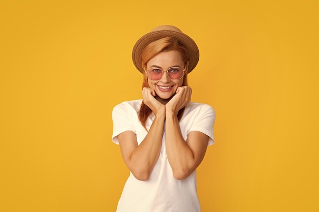 Retrato sorridente de uma jovem bonita usando óculos escuros e chapéu de palha sobre fundo amarelo Garota feliz aproveitando o verão