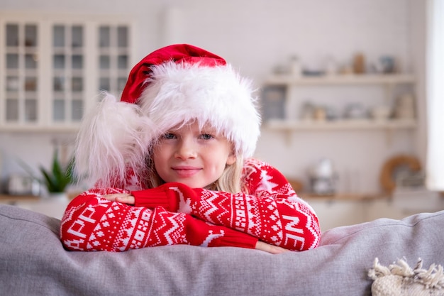 Retrato sorridente esperando a garota de férias com chapéu de Papai Noel e fantasia de Natal sentado em casa