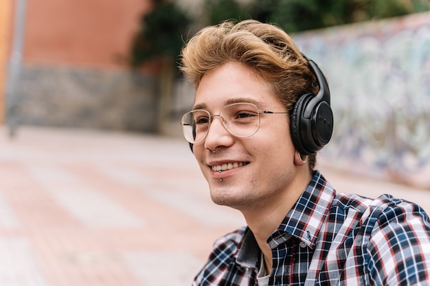 Retrato sorridente jovem com óculos está ouvindo música em fones de ouvido