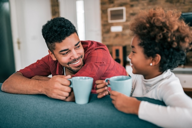 Retrato de un té de consumición del padre joven feliz con su hija en casa.