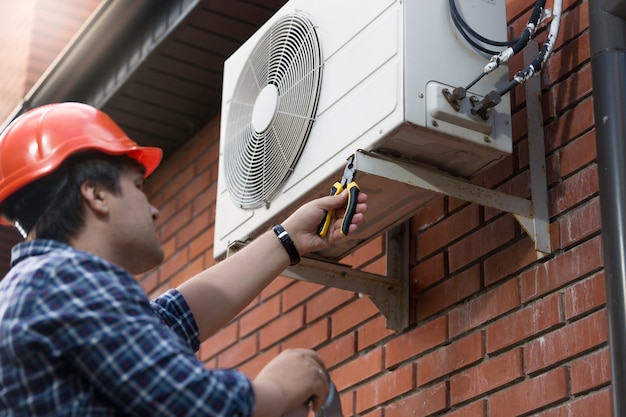 Retrato de técnico en casco conectando la unidad de aire acondicionado  exterior