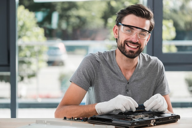 Foto retrato de un técnico de sexo masculino joven feliz que repara la computadora