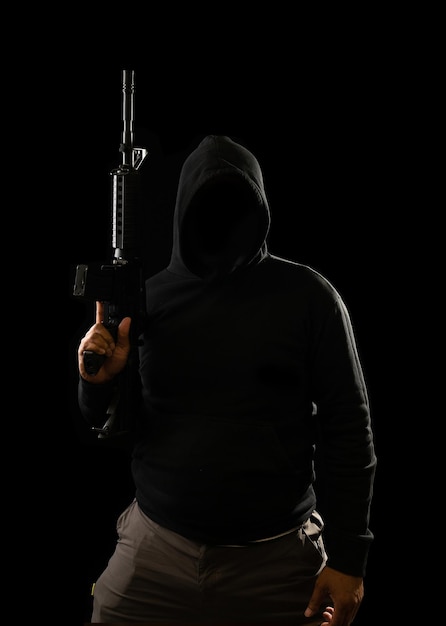 Retrato de un terrorista con una capucha negra sosteniendo un fusil m16: concepto de terrorismo