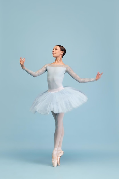 Retrato de tierna joven bailarina bailando aislado sobre fondo azul de estudio de pie