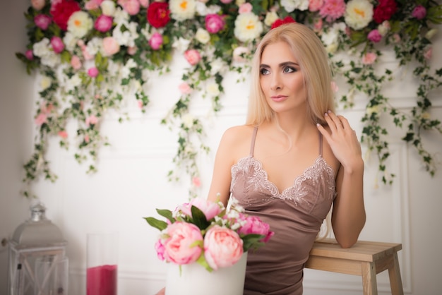 Retrato de una tierna joven bastante rubia posando sobre un fondo de flores de colores vivos borrosos y una pared blanca. Concepto de feminidad y belleza