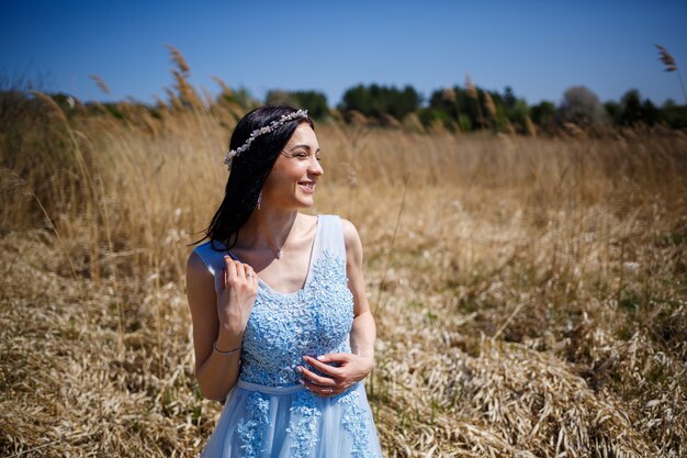 Retrato de una tierna niña en un vestido largo azul en guisantes secos con una sonrisa en su rostro en un cálido día de verano soleado