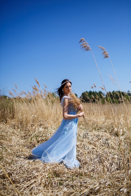 Retrato de una tierna niña en un vestido largo azul en guisantes secos con una sonrisa en su rostro en un cálido día de verano soleado