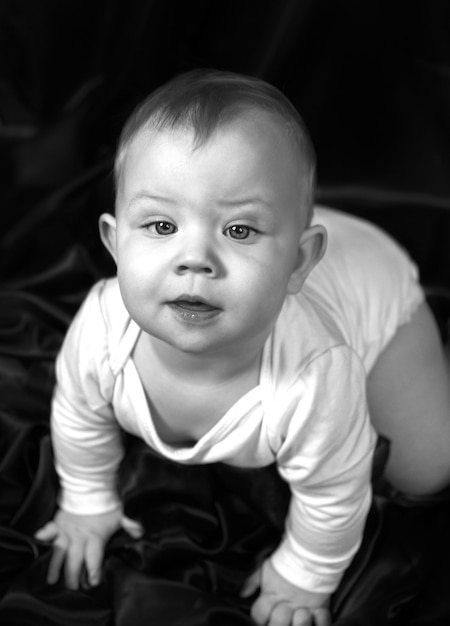 Retrato tierno en blanco y negro de un bebé de un año desde arriba El niño se para a cuatro patas sobre un paño negro levantando la cabeza mirando a la cámara