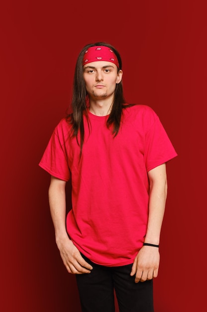 Retrato de un tipo positivo con una banda roja en la cabeza y una camisa de pie contra la pared roja