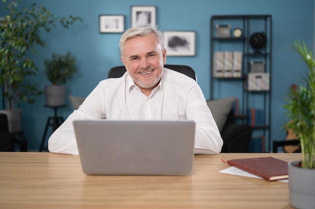 Retrato de un tipo sonriente feliz en su s trabajando en una computadora portátil en la sala de estar en casa