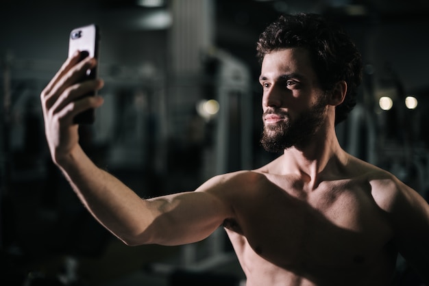 Retrato de tiro medio de confiado joven barbudo tomando foto selfie en smartphone