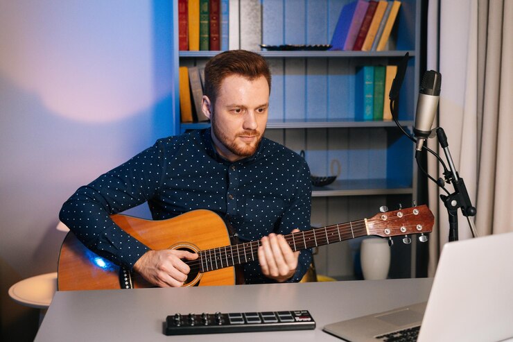 Foto retrato de tiro medio de un joven guitarrista aprendiendo guitarra en una clase de música en línea con un maestro distante sentado en el escritorio mirando la pantalla de una computadora portátil músico creativo que tiene actividades de ocio relajándose solo