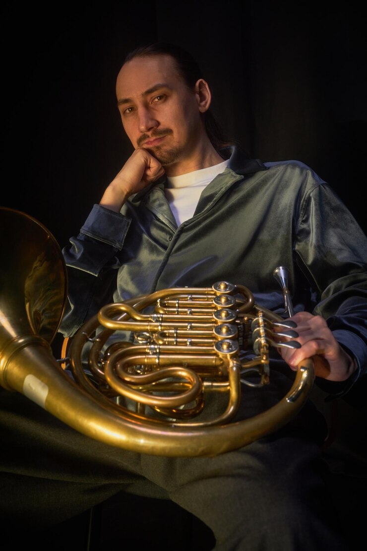 Foto retrato de un tocador de cuerno francés posando con un instrumento sentado en un estudio débilmente iluminado