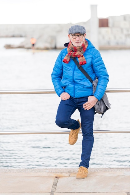 Foto retrato en toda su longitud de un anciano de pie en el muelle frente al mar