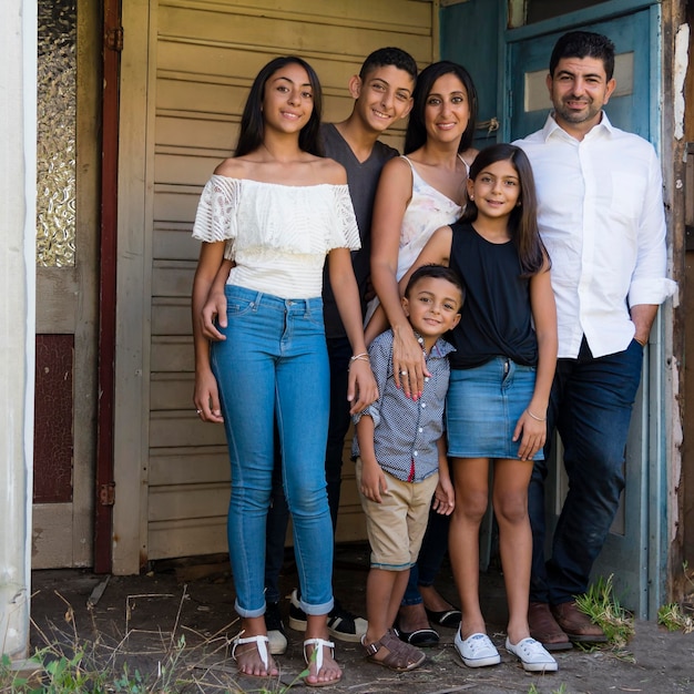 Foto retrato en toda su longitud de una familia sonriente de pie contra la casa