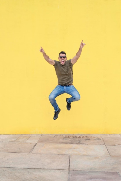 Foto retrato en toda su longitud de un hombre alegre saltando contra una pared amarilla