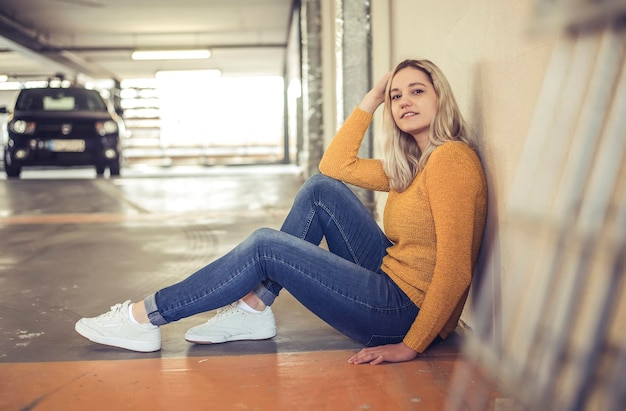 Retrato en toda su longitud de una mujer joven sentada en un estacionamiento subterráneo