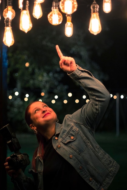 Foto retrato en toda su longitud de una mujer joven sosteniendo un equipo de iluminación iluminado por la noche