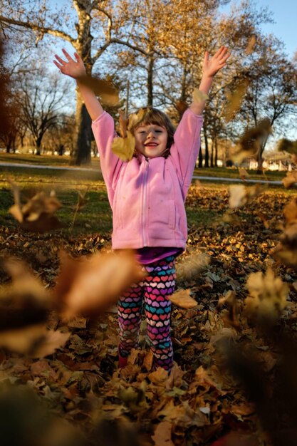 Foto retrato en toda su longitud de una niña arrojando hojas en el campo