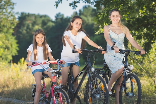 Retrato tonificado de duas irmãs pedalando com a mãe em um prado à beira do lago