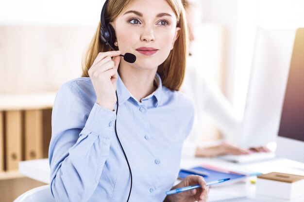 Retrato tonificado do operador de call center no trabalho. Grupo de pessoas em um fone de ouvido pronto para ajudar os clientes. Conceito de negócios.