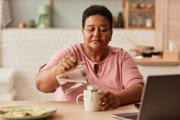 Retrato en tonos cálidos de una anciana negra haciendo té durante el desayuno en una cocina acogedora