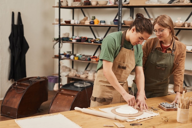 Retrato de tonos cálidos de dos jóvenes haciendo cerámica mientras trabajaba en el taller de cerámica, concepto de pequeña empresa, espacio de copia
