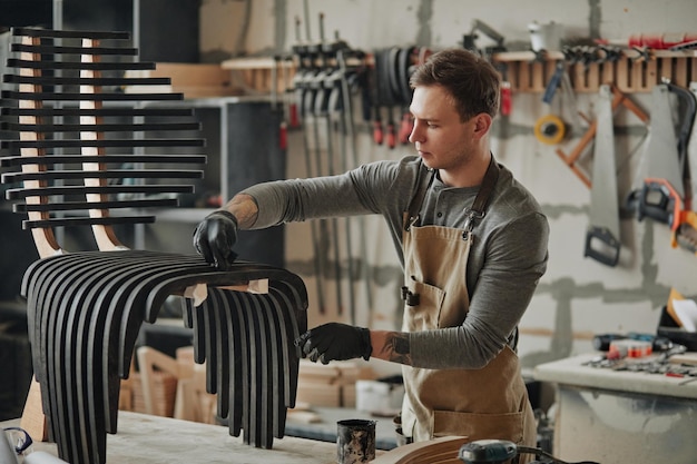 Retrato en tonos cálidos de un joven carpintero construyendo muebles de madera de diseñador en el espacio de copia del taller