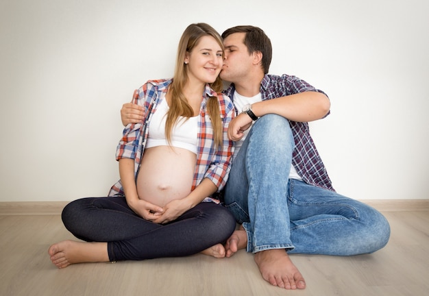 Retrato de tonos de feliz pareja embarazada sentada en el suelo y besos